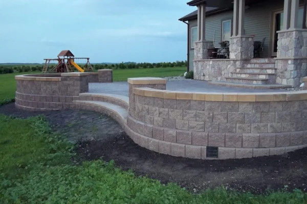 Backyard scene with a stone patio, a playground set, and an adjacent house with a stone porch.