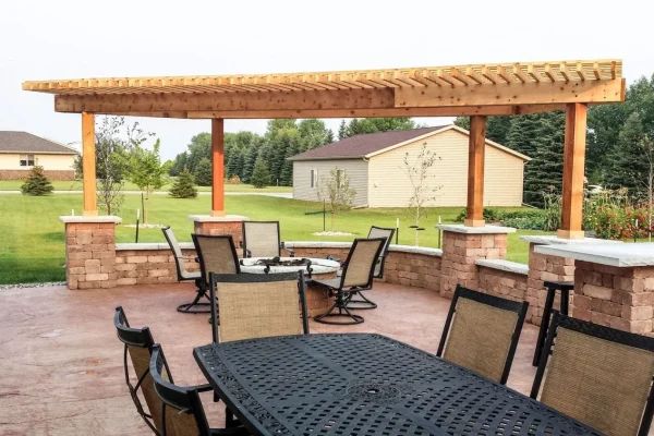 Patio with a wooden pergola and black metal table surrounded by wicker chairs. | Landscaping and Outdoor Living Services