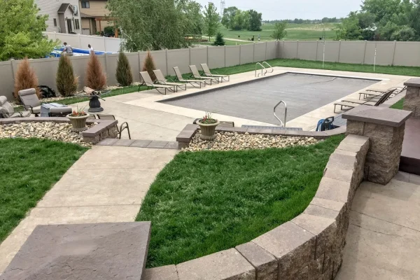A backyard featuring a swimming pool surrounded by a patio area with outdoor furniture and greenery.