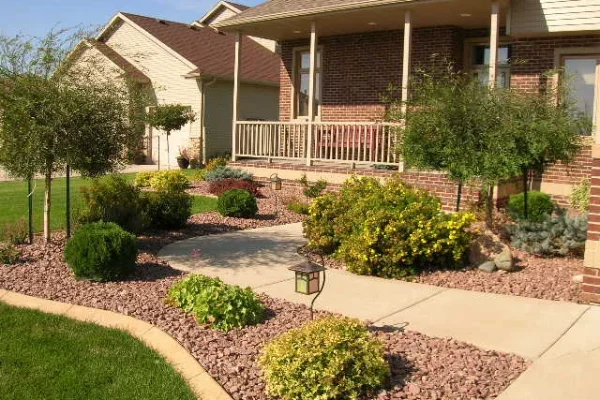Front yard garden with shrubs, a concrete path, and solar lamps leading to a brick house with a porch.