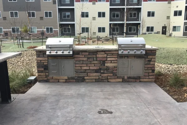 An outdoor kitchen featuring two grills set against a rustic brick wall, ideal for cooking and entertaining.